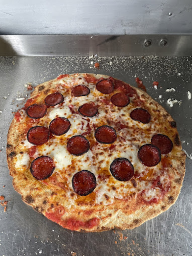 A Fables pepperoni pizza with melted cheese and a browned crust on a metal preparation counter.